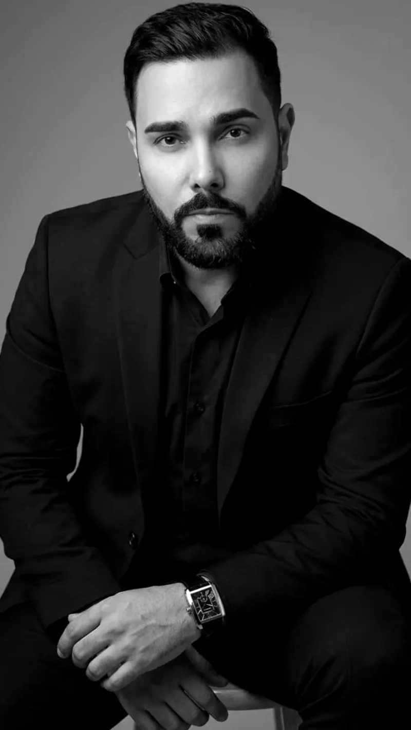 Retrato de estúdio do advogado, de terno preto e relógio, sentado, fundo cinza, em preto e branco