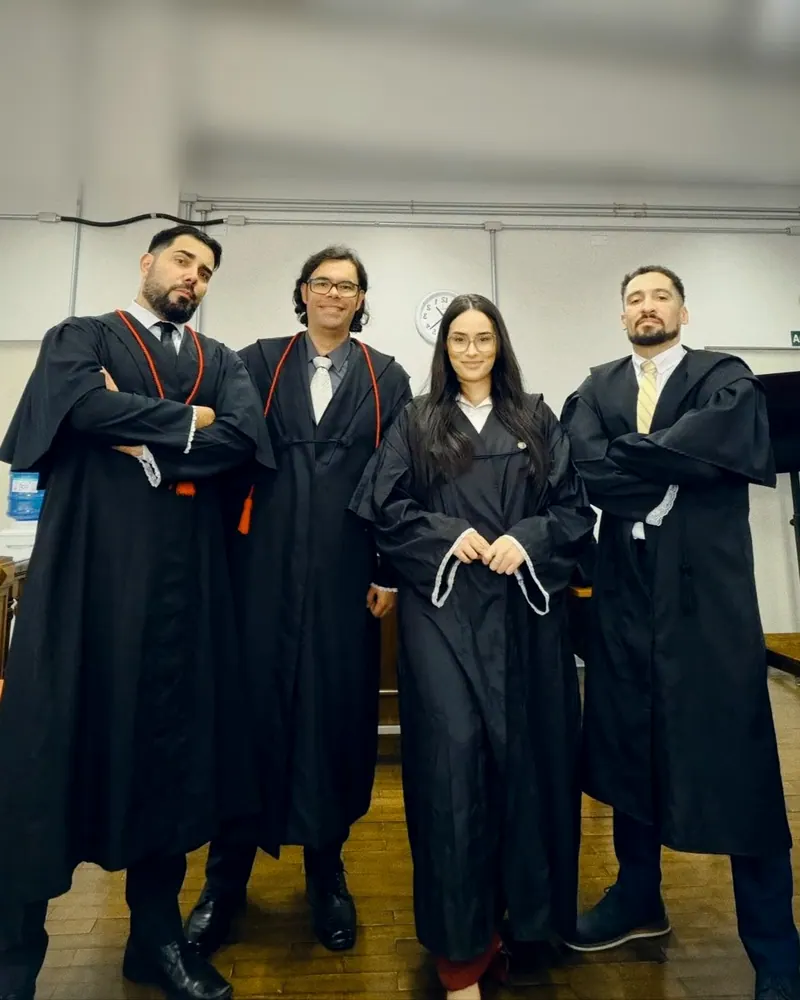 Quatro advogados de toga posando lado a lado na sala de audiência, o Sandro à esquerda de braços cruzados
